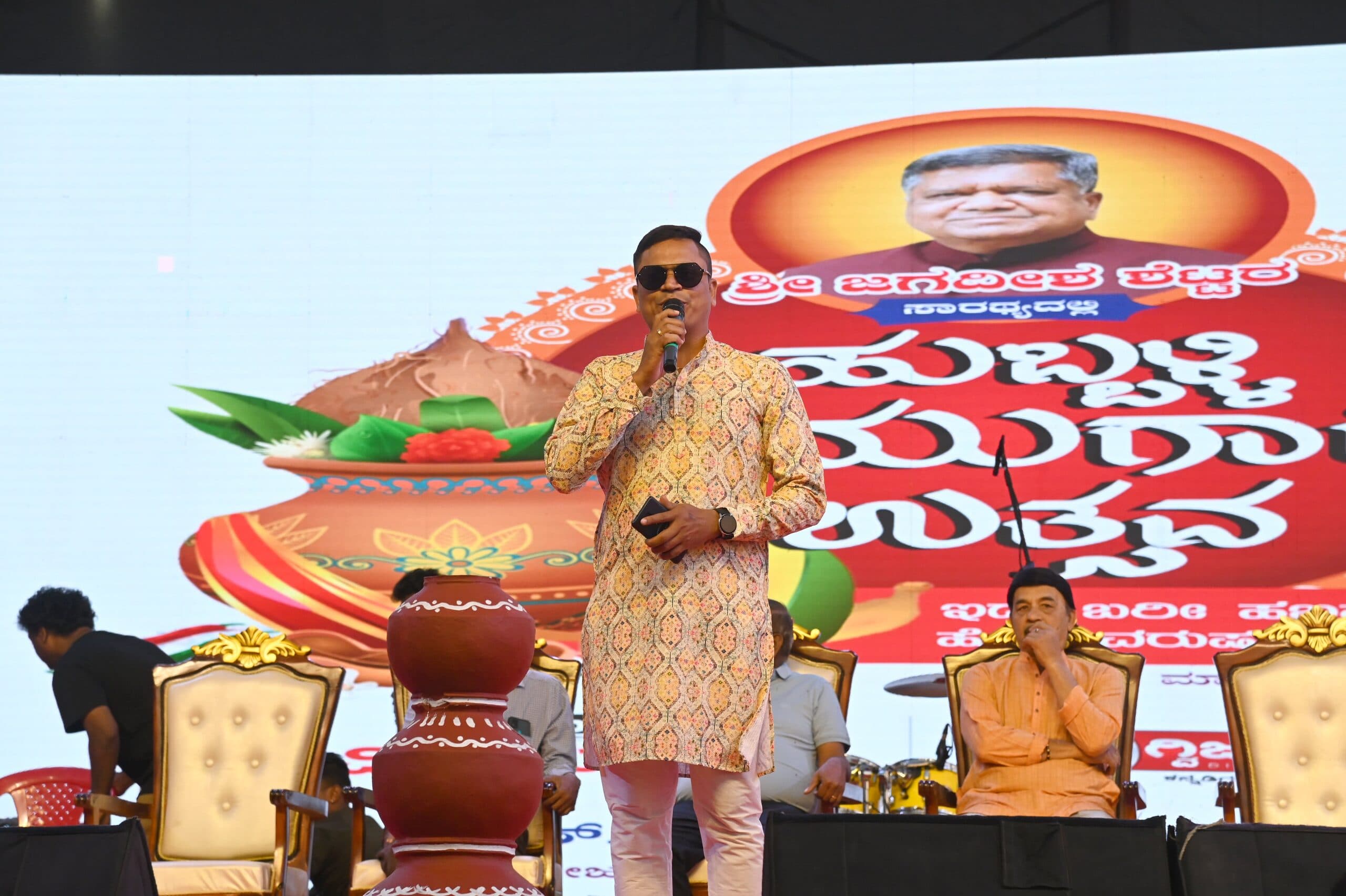 Host on stage in front of a giant Ugadi wordmark and a kalash prop