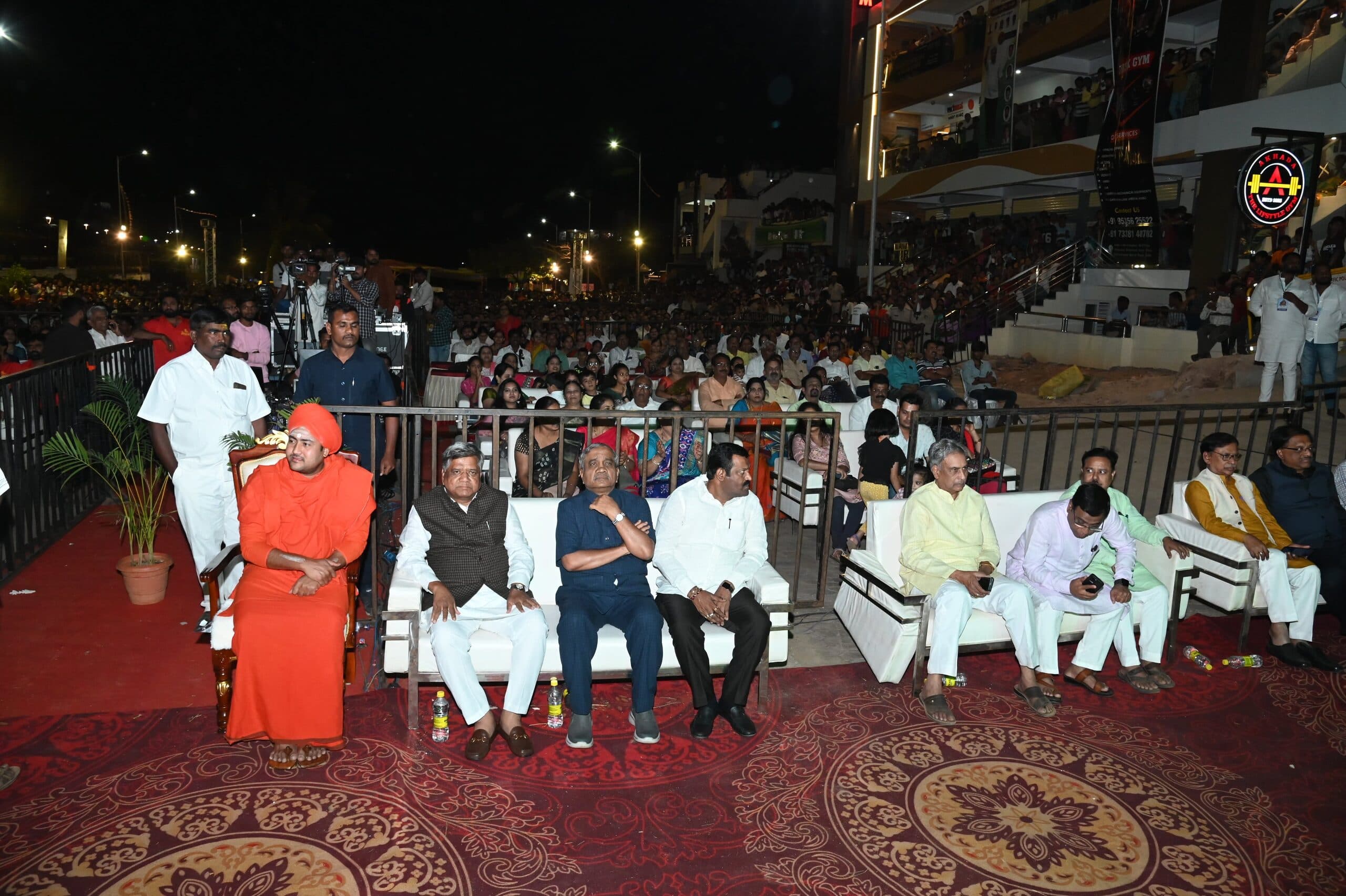 Front-row guests seated beside the stage as the night crowd fills the ground behind