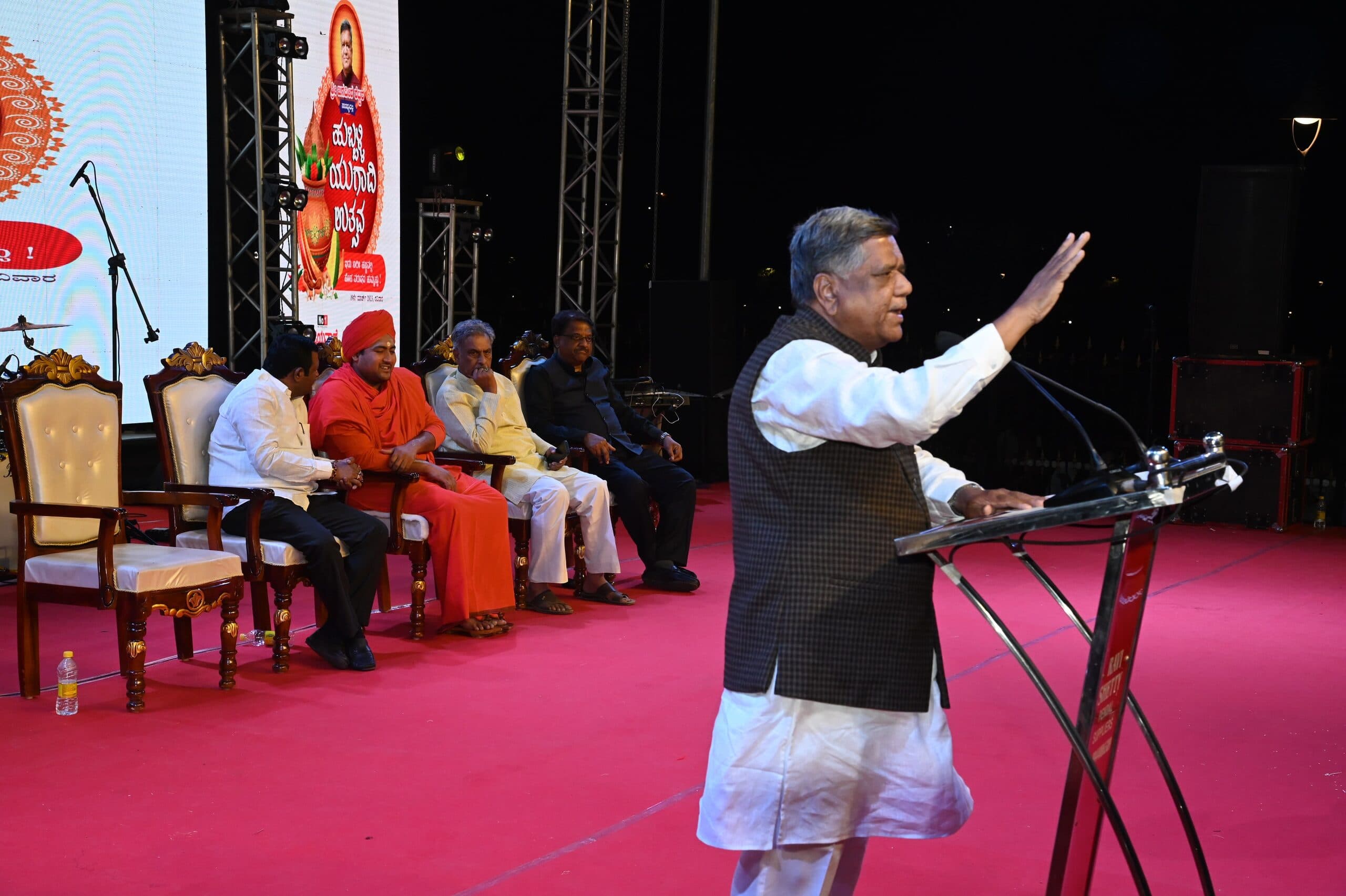 Speaker at the lectern on the red-carpeted stage with seated guests behind him
