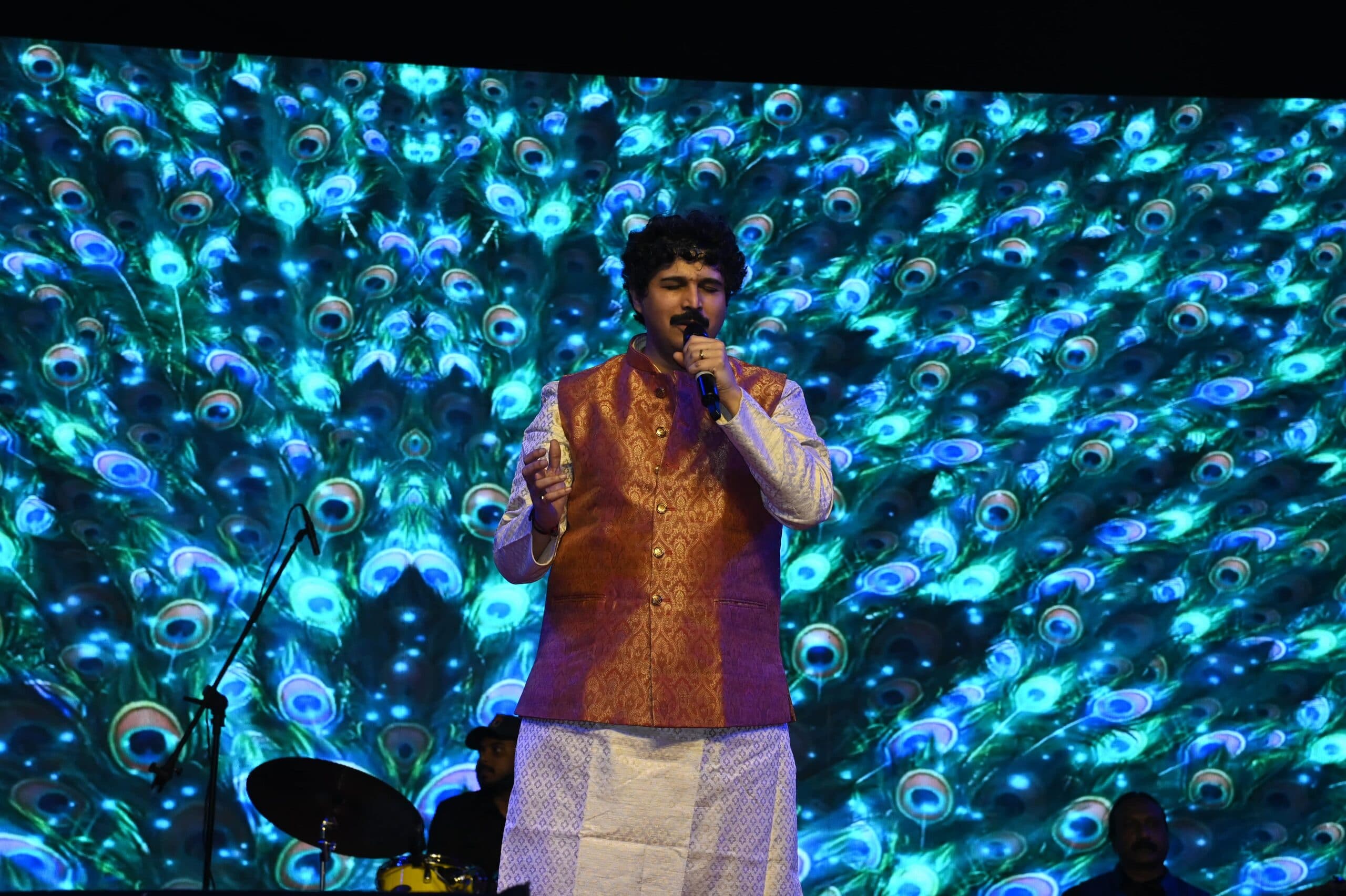 A vocalist mid-performance in front of a peacock-feather LED wall
