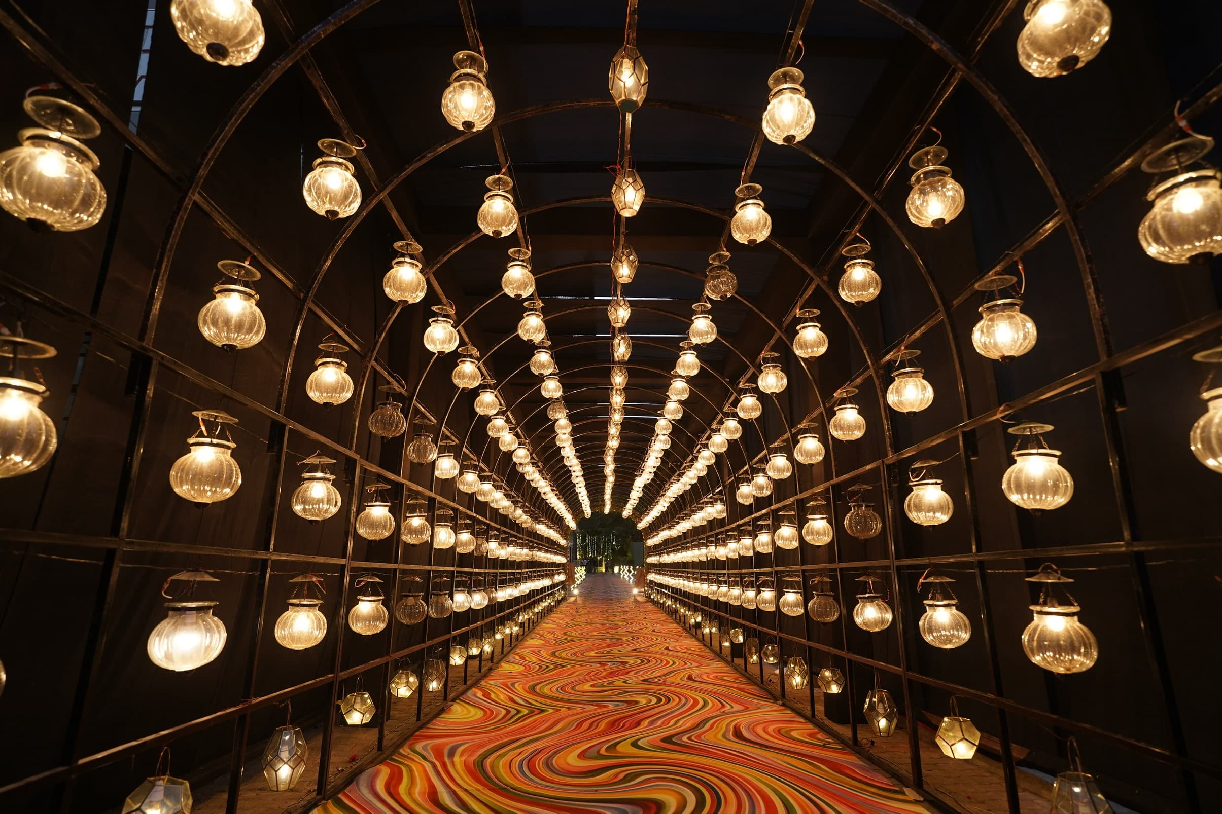 A guest walkway roofed with hundreds of hanging glass bulbs over a swirling patterned carpet