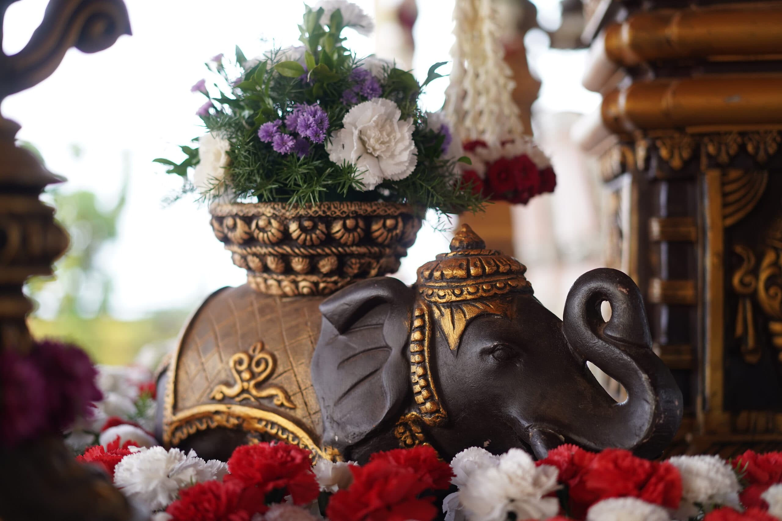 A carved brass elephant and a flower-filled urn set into a wedding mandap