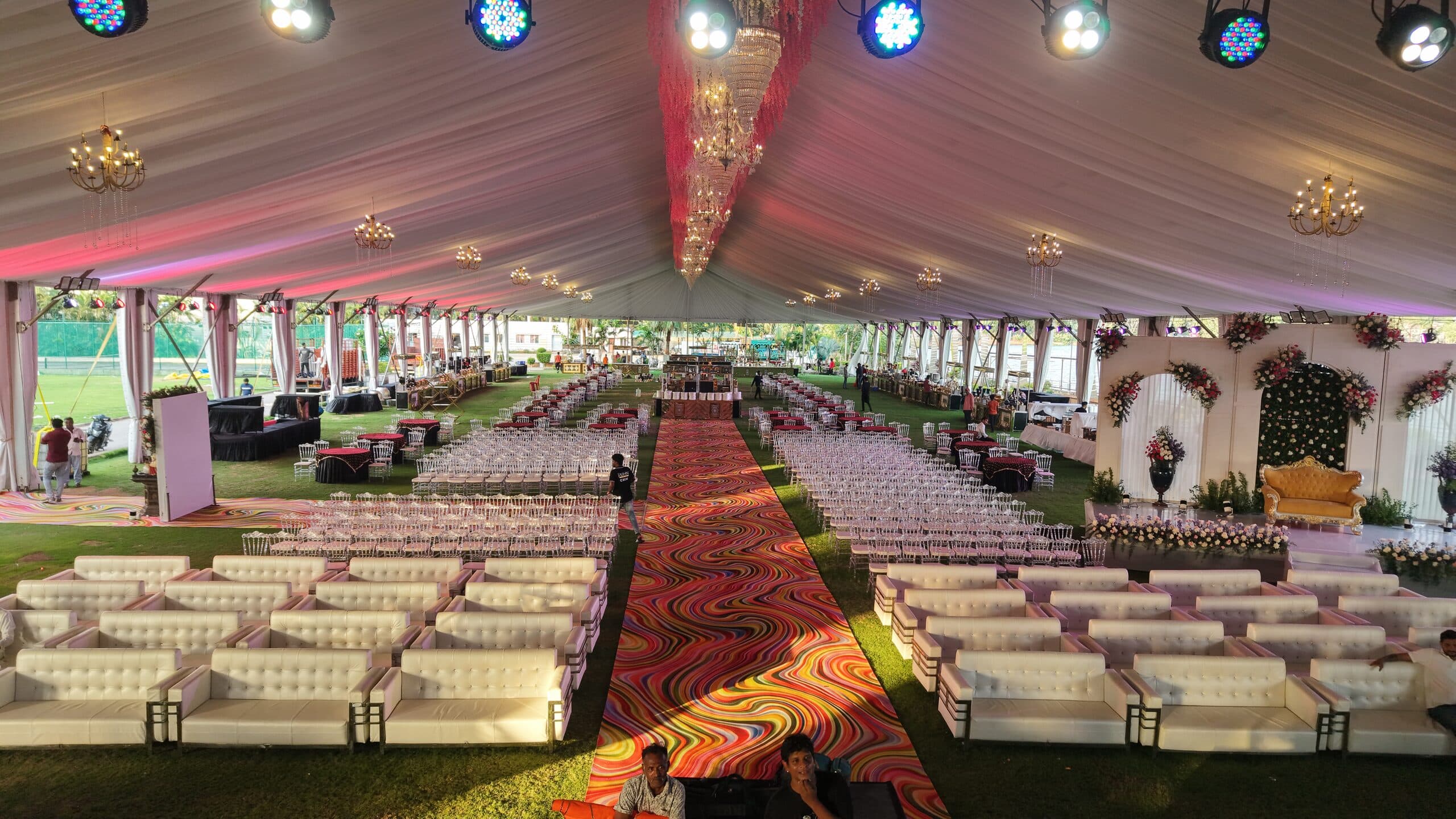 Rows of white lounge seating either side of a patterned carpet aisle inside a draped marquee