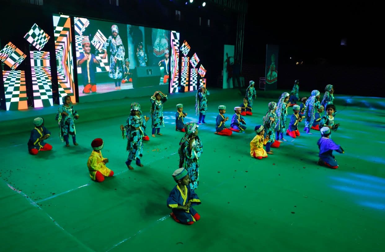 Children performing in costume across a green-lit performance stage