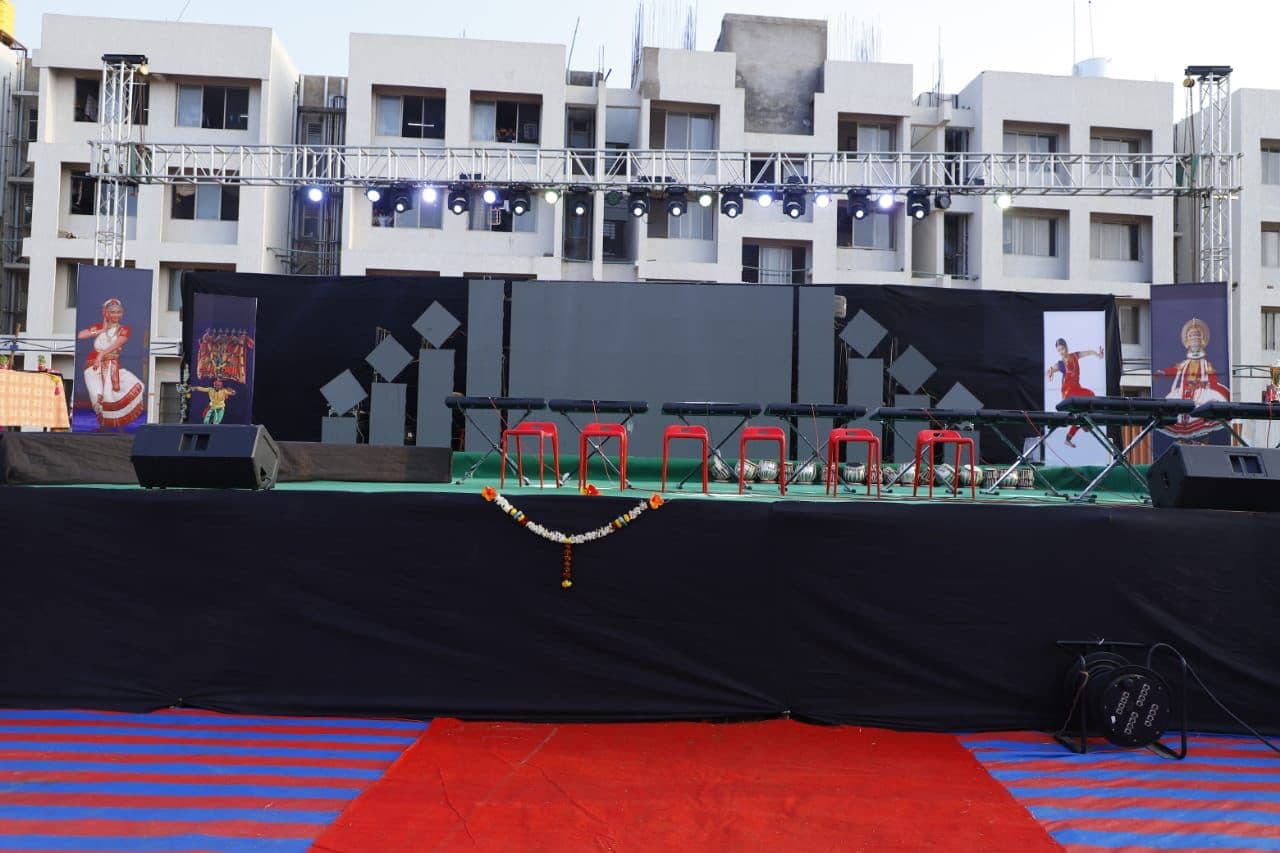 Black open-air stage with a red carpet apron in front of apartment blocks