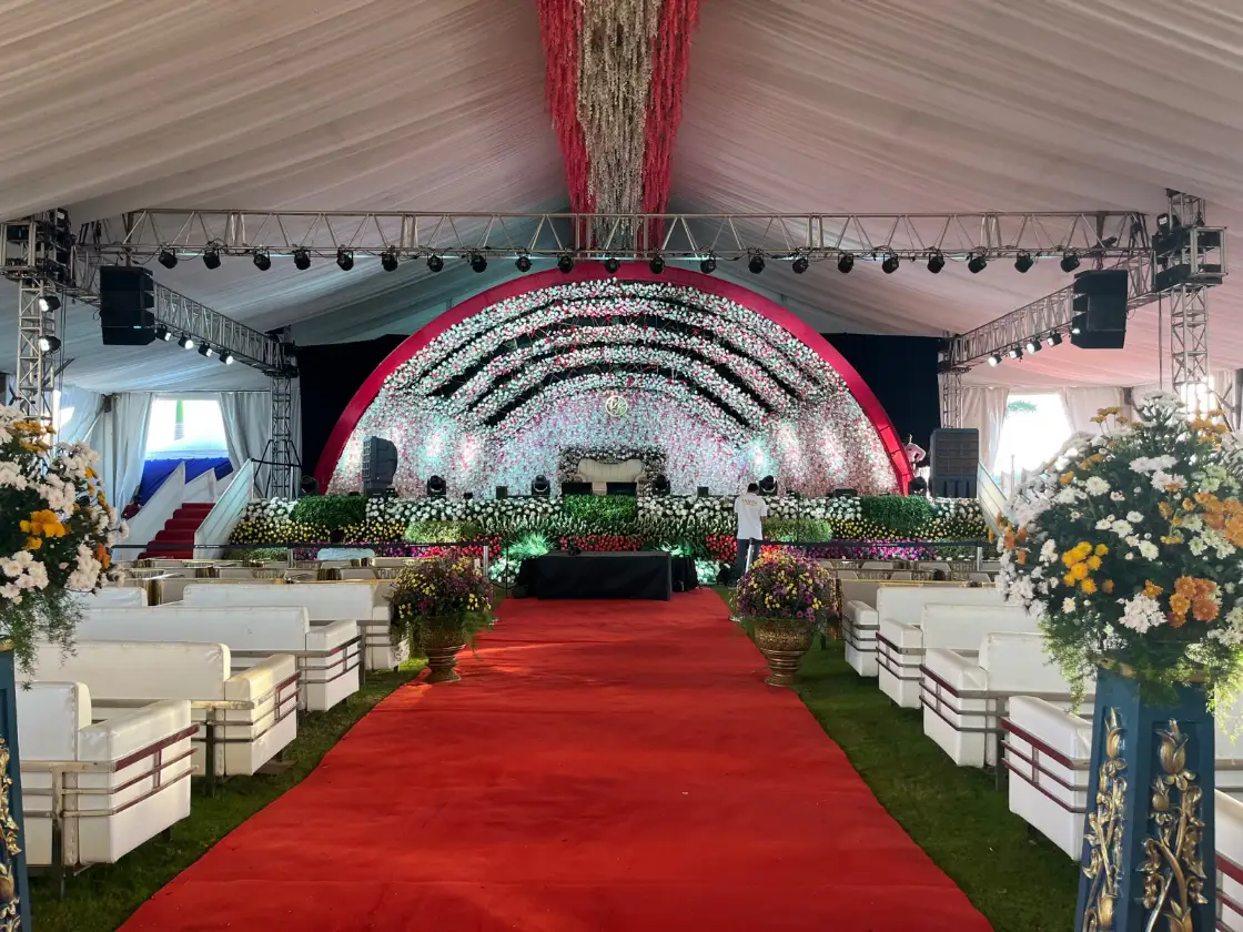 A wedding reception stage framed by a floral arch and a red-carpet aisle