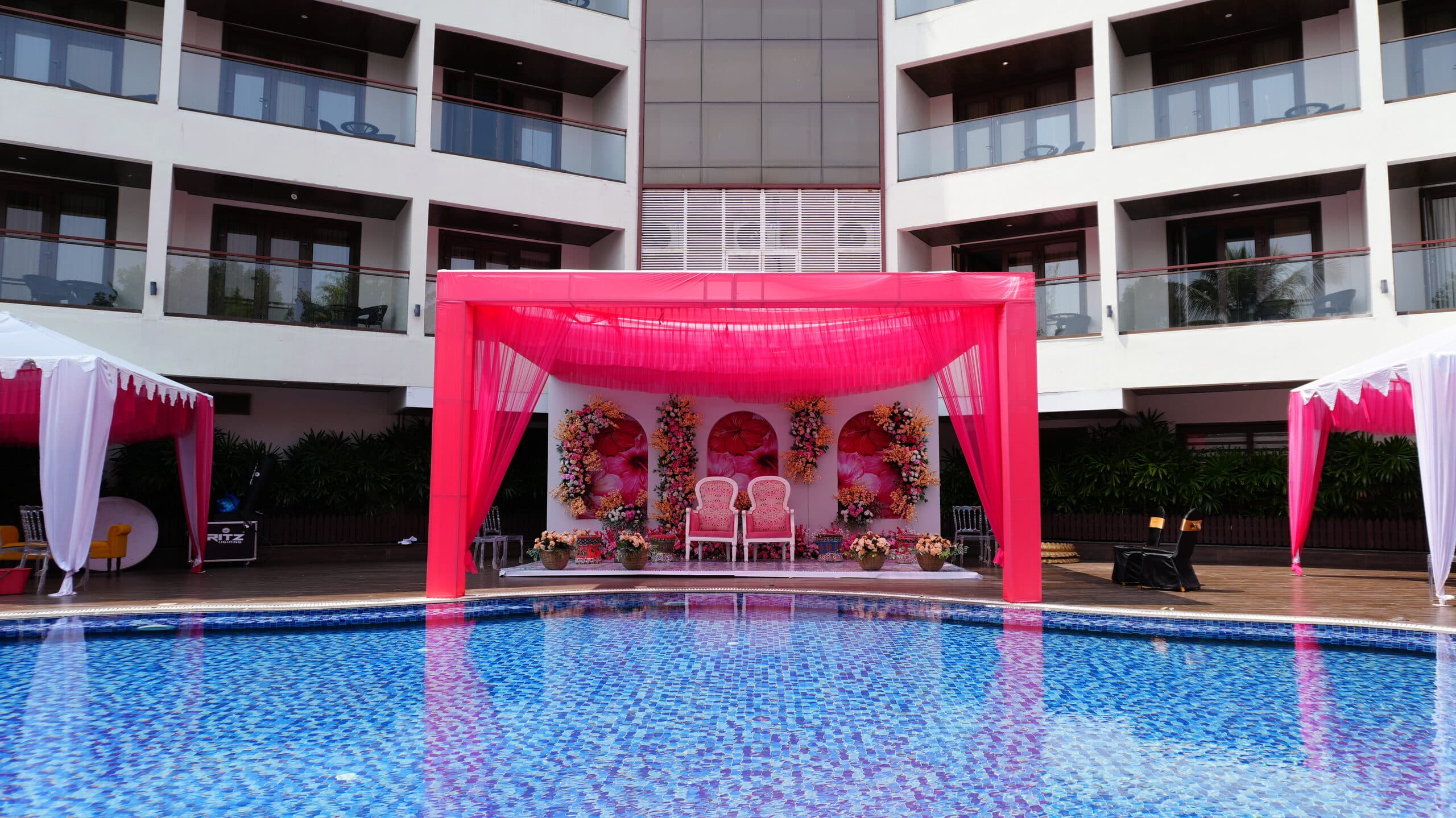 Pink draped poolside mandap with blush chairs, mirrored in the pool below the hotel façade
