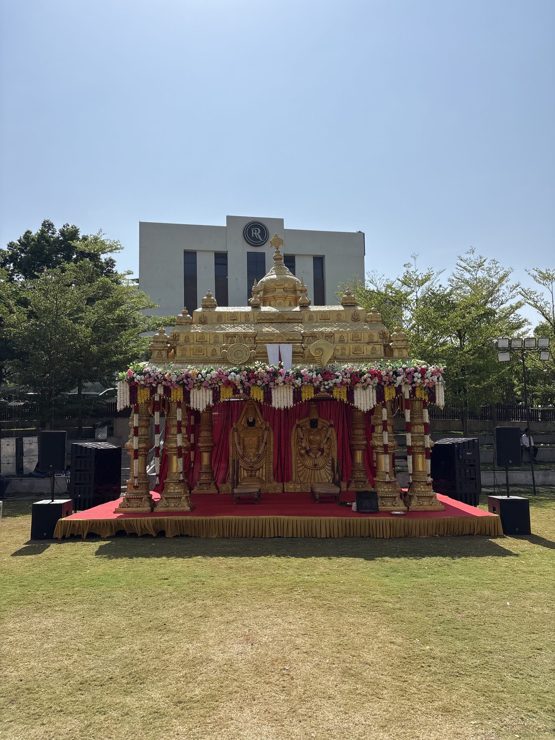 Carved gold temple mandap raised on a red platform on the open lawn