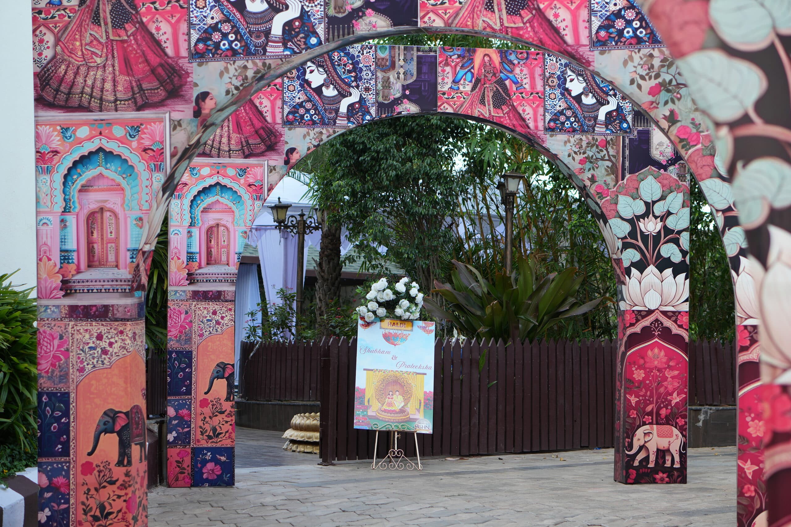 Hand-painted arch gateway in pink and blue with elephant motifs, opening onto the haldi lawn