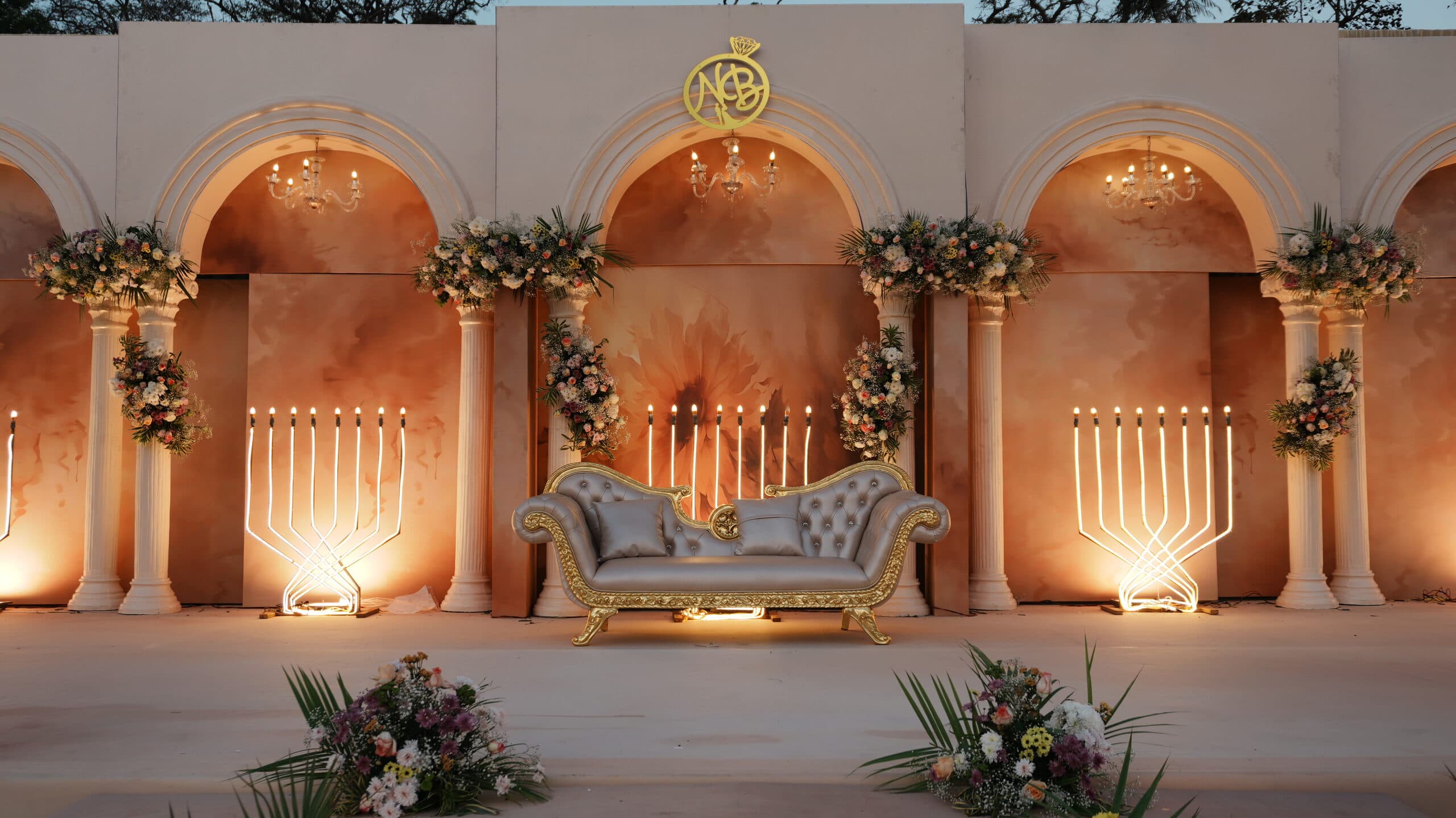 Peach and gold arched stage with candelabra, a monogrammed crest and a cream settee