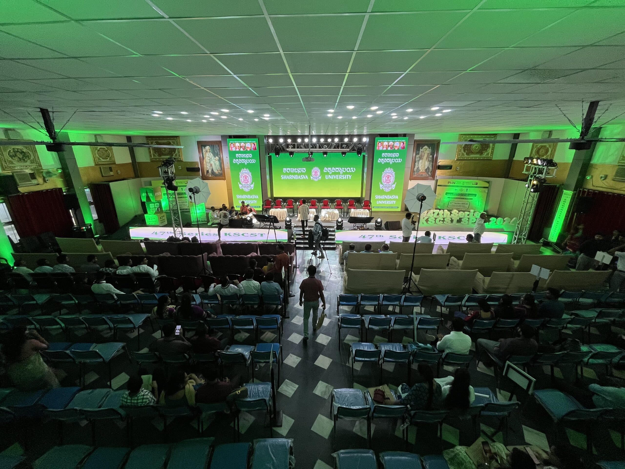 Delegates seated in rows down the hall toward the green-lit presentation stage
