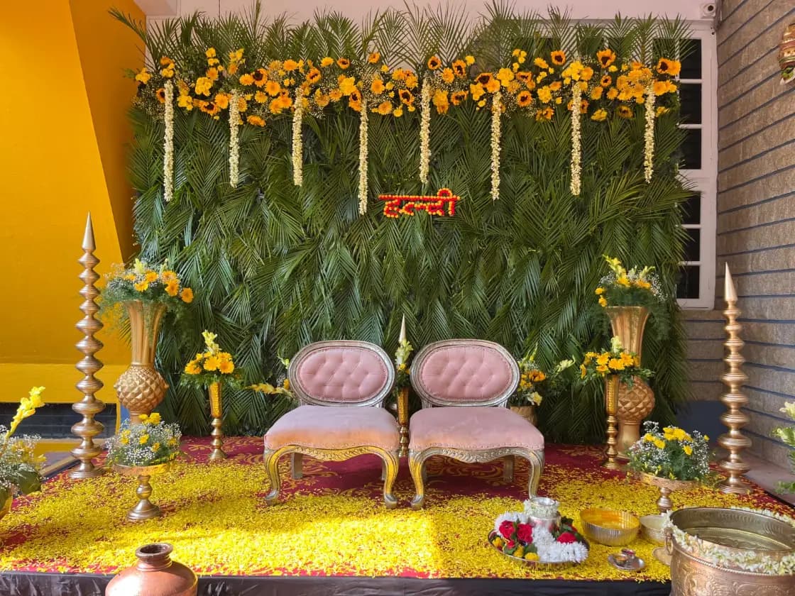 A haldi stage of marigolds and palm fronds with two blush velvet chairs